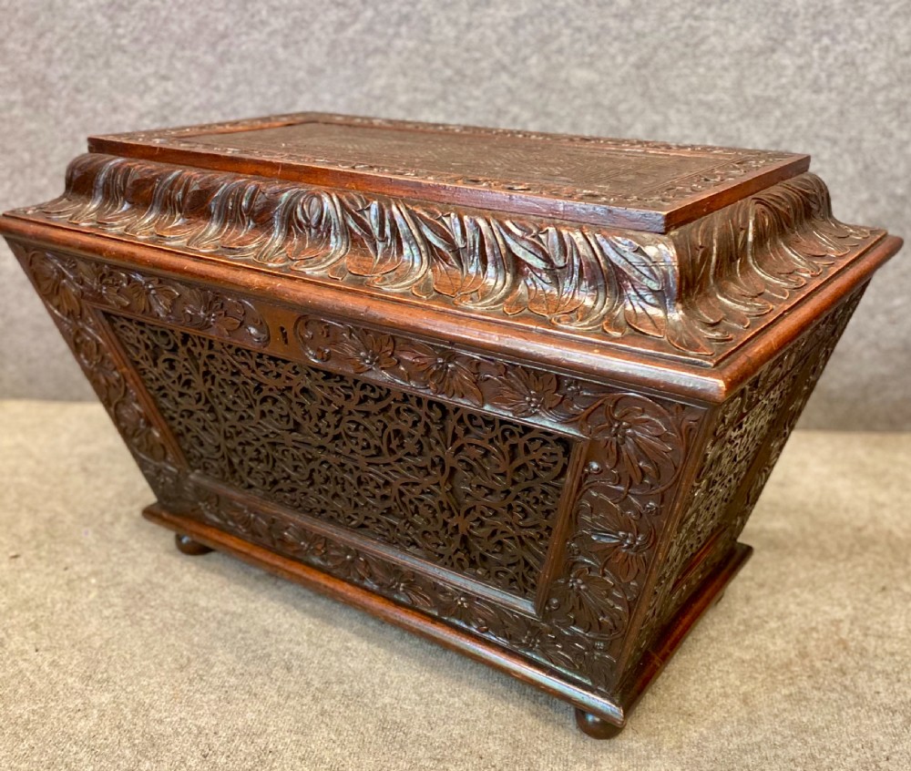 A dark hardwood Anglo-Indian carved cellarette featuring detailed floral latticework, a sarcophagus lid, and small ball feet.