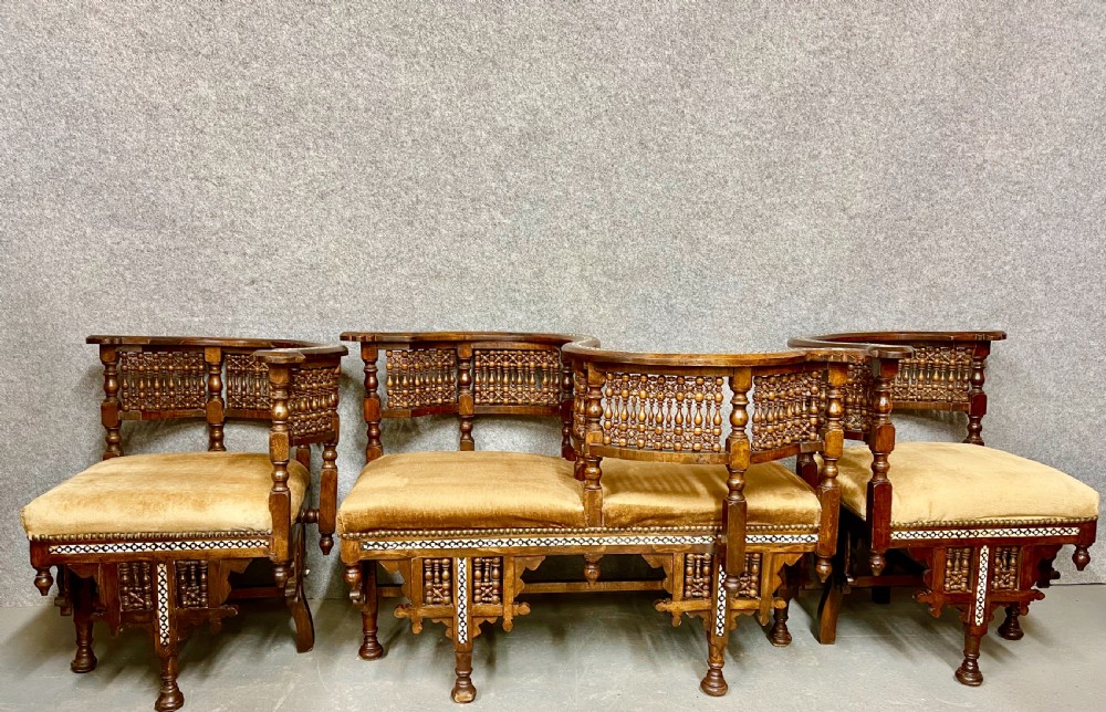 A dark hardwood Moorish Revival seating suite consisting of an S-shaped central conversation seat flanked by two corner armchairs, embellished with lathe-turned spindle lattice backs, geometric bone inlay, and mustard velvet seats.