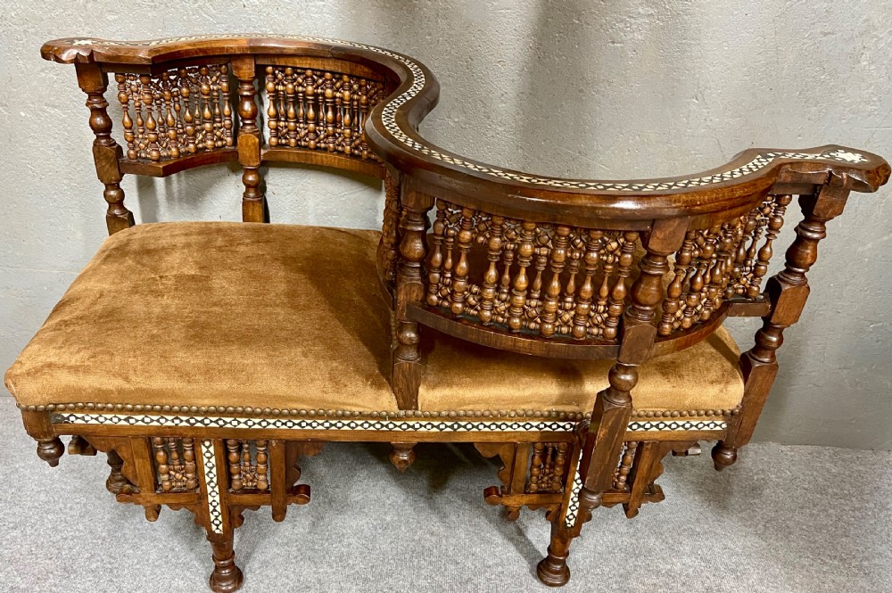 A dark hardwood Moorish Revival seating suite consisting of an S-shaped central conversation seat flanked by two corner armchairs, embellished with lathe-turned spindle lattice backs, geometric bone inlay, and mustard velvet seats. View III