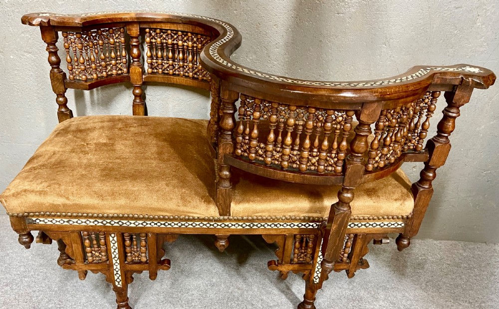 A dark hardwood Moorish Revival seating suite consisting of an S-shaped central conversation seat flanked by two corner armchairs, embellished with lathe-turned spindle lattice backs, geometric bone inlay, and mustard velvet seats. View VII