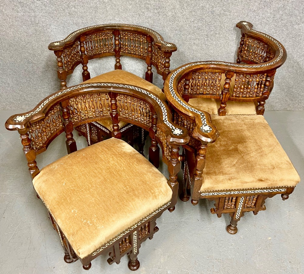A dark hardwood Moorish Revival seating suite consisting of an S-shaped central conversation seat flanked by two corner armchairs, embellished with lathe-turned spindle lattice backs, geometric bone inlay, and mustard velvet seats. View VIII