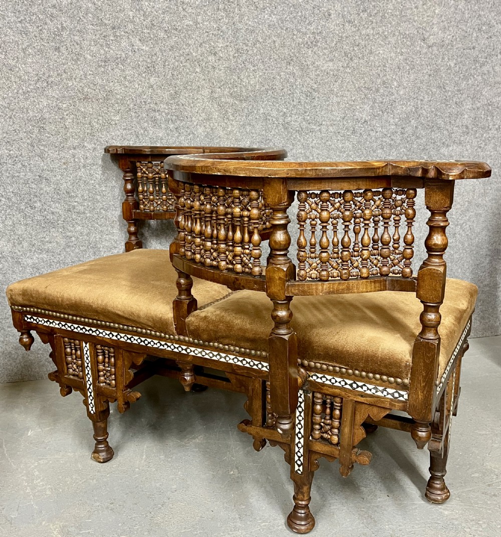 A dark hardwood Moorish Revival seating suite consisting of an S-shaped central conversation seat flanked by two corner armchairs, embellished with lathe-turned spindle lattice backs, geometric bone inlay, and mustard velvet seats. View IX
