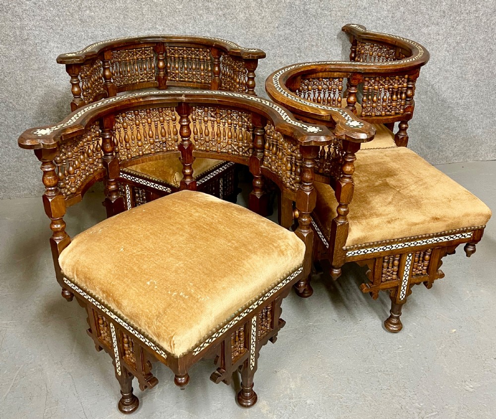 A dark hardwood Moorish Revival seating suite consisting of an S-shaped central conversation seat flanked by two corner armchairs, embellished with lathe-turned spindle lattice backs, geometric bone inlay, and mustard velvet seats. View X