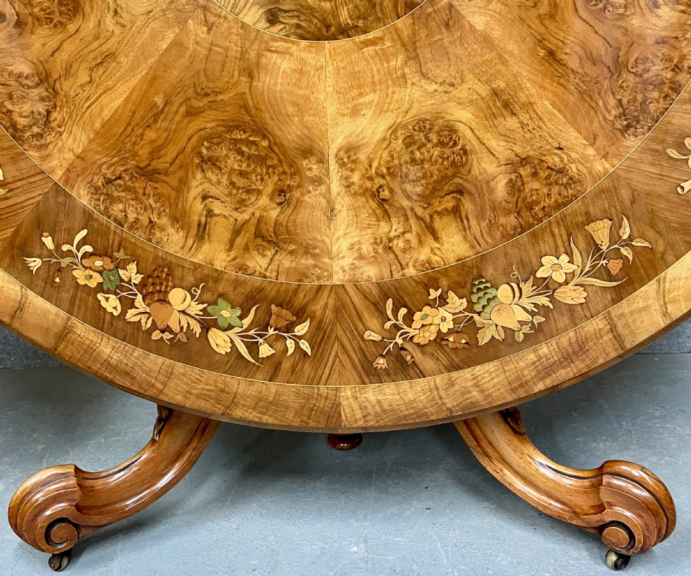 A circular Victorian burr walnut centre table featuring floral marquetry inlay on the top surface and supported by a carved pedestal base. View III