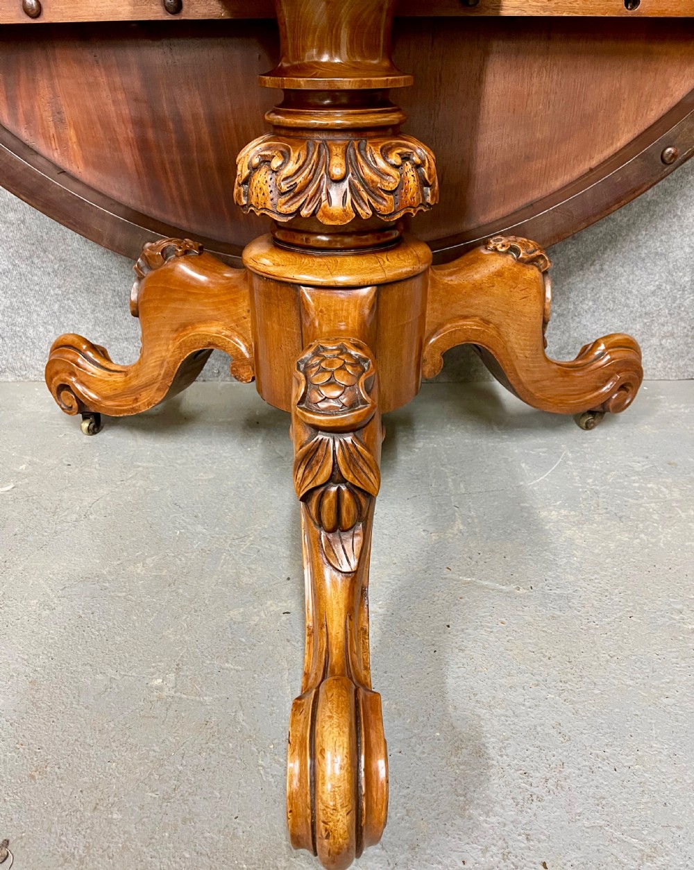 A circular Victorian burr walnut centre table featuring floral marquetry inlay on the top surface and supported by a carved pedestal base. View VI