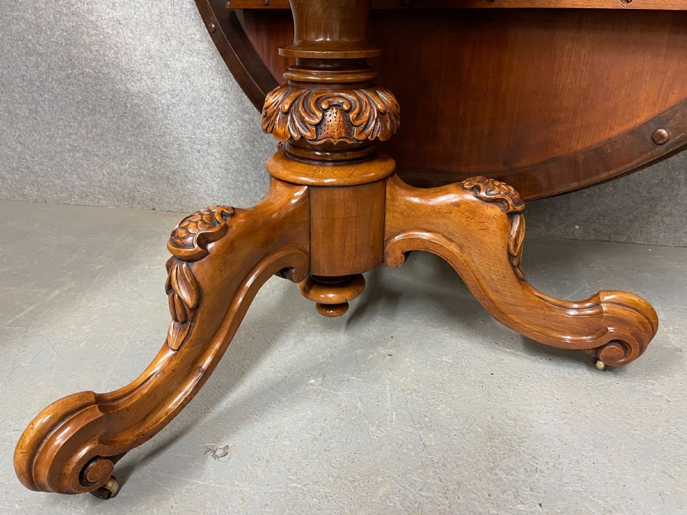 A circular Victorian burr walnut centre table featuring floral marquetry inlay on the top surface and supported by a carved pedestal base. View VIII