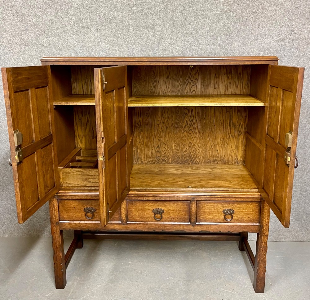 A warm brown oak cocktail cabinet featuring three carved panel doors above three drawers, set on a sturdy base with square legs. View III