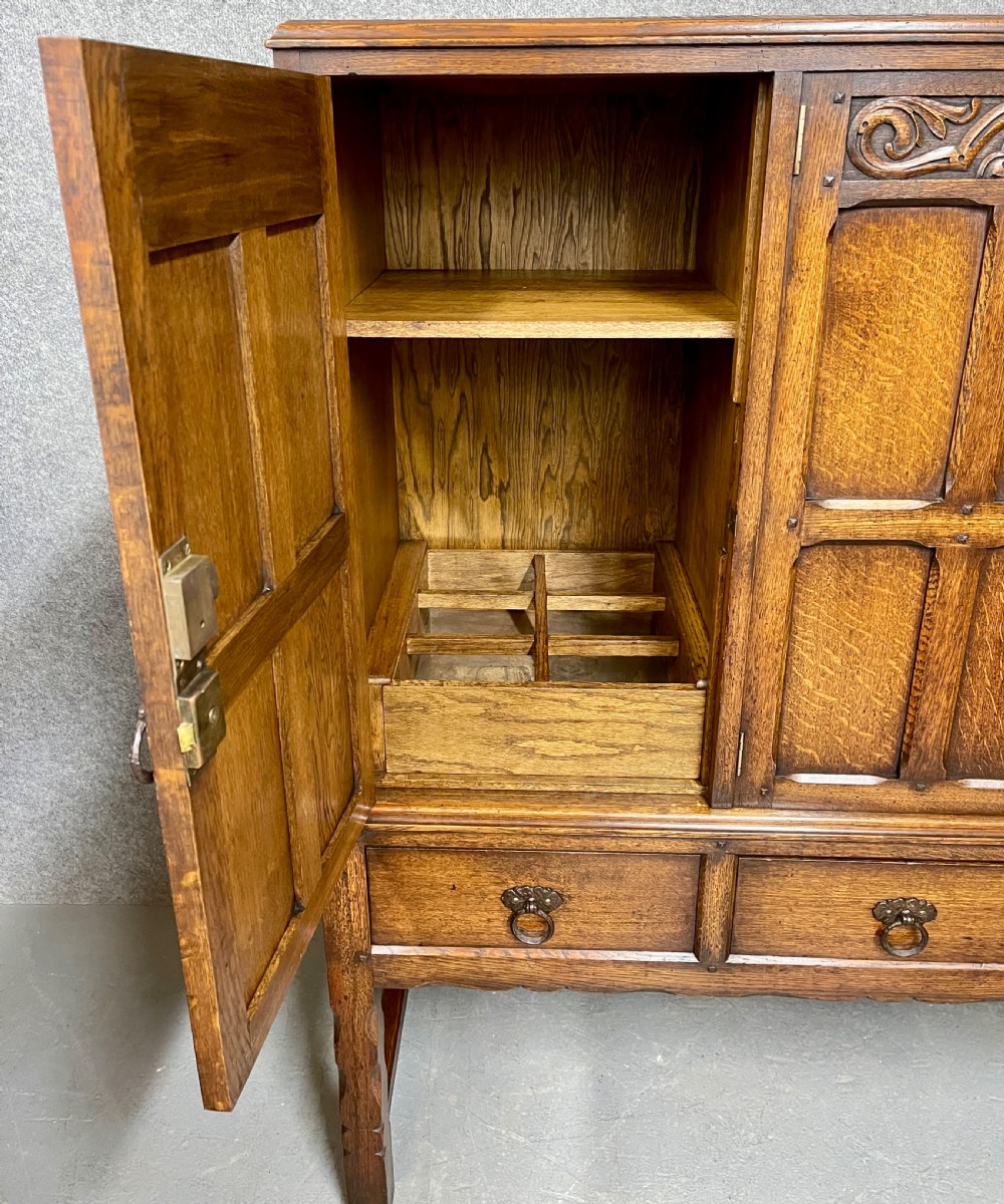 A warm brown oak cocktail cabinet featuring three carved panel doors above three drawers, set on a sturdy base with square legs. View V