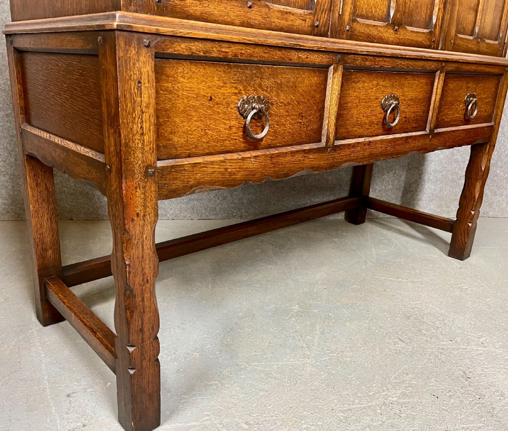 A warm brown oak cocktail cabinet featuring three carved panel doors above three drawers, set on a sturdy base with square legs. View VI