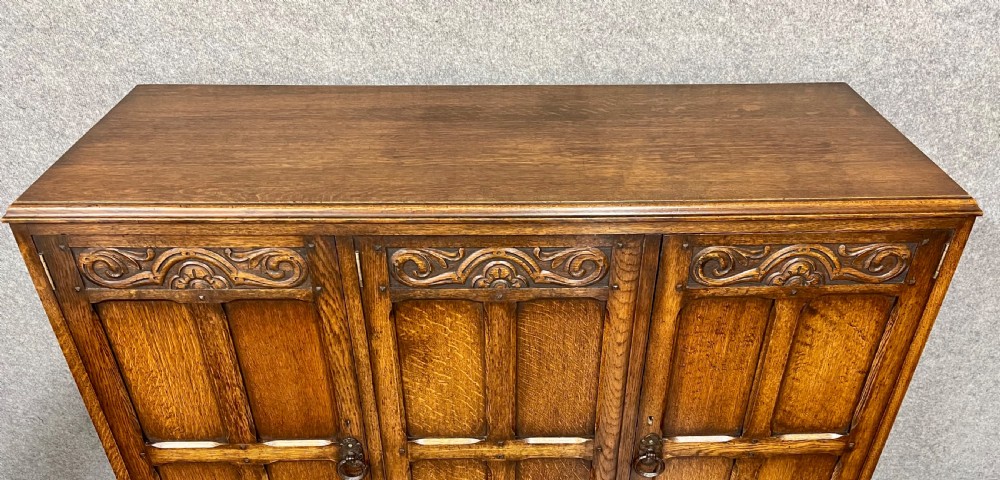 A warm brown oak cocktail cabinet featuring three carved panel doors above three drawers, set on a sturdy base with square legs. View VII