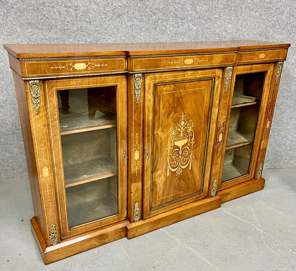 A Victorian warm brown walnut credenza featuring a central inlaid panel door flanked by two glazed display cabinet doors with gilt metal mounts.