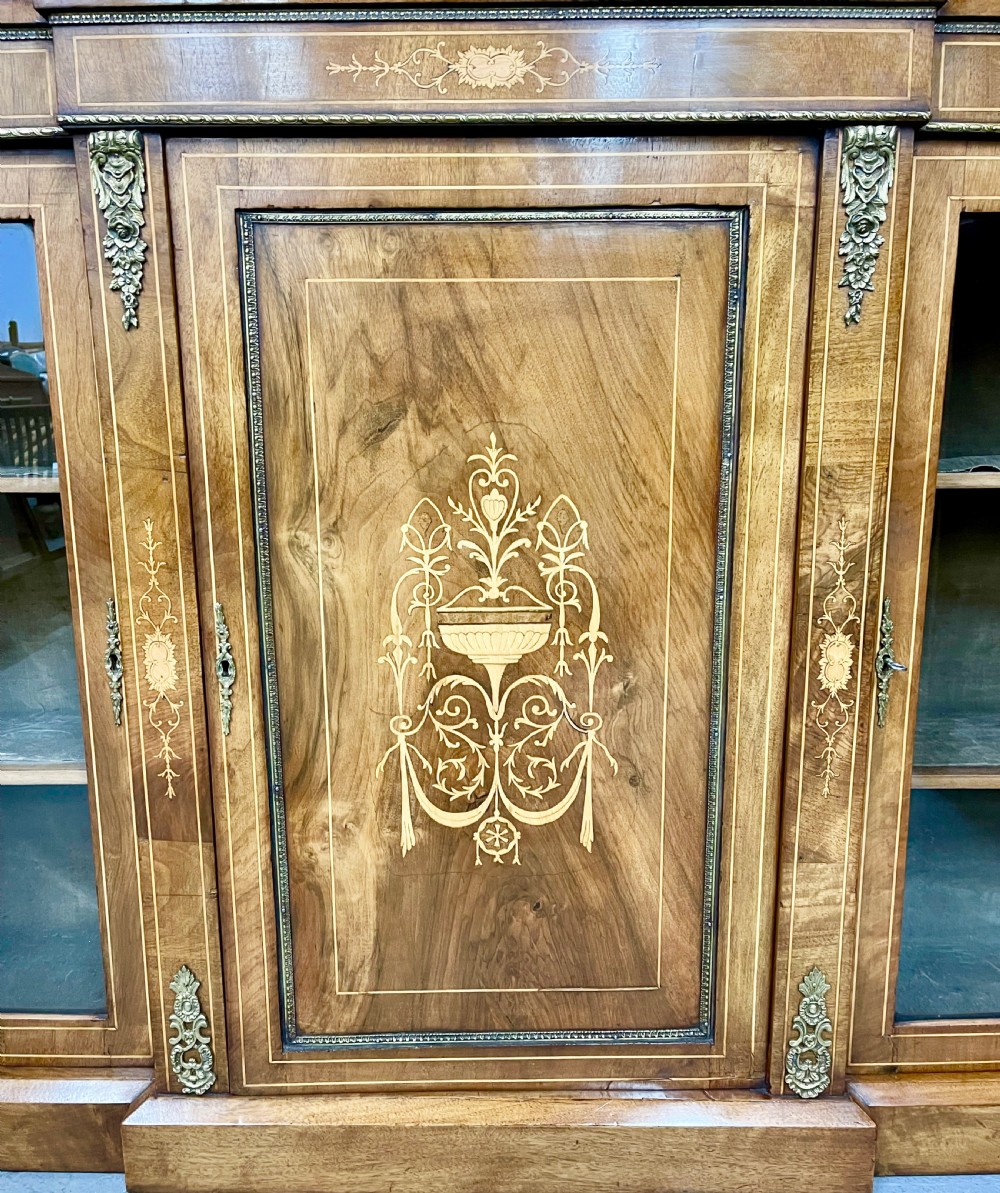 A Victorian warm brown walnut credenza featuring a central inlaid panel door flanked by two glazed display cabinet doors with gilt metal mounts. View VI