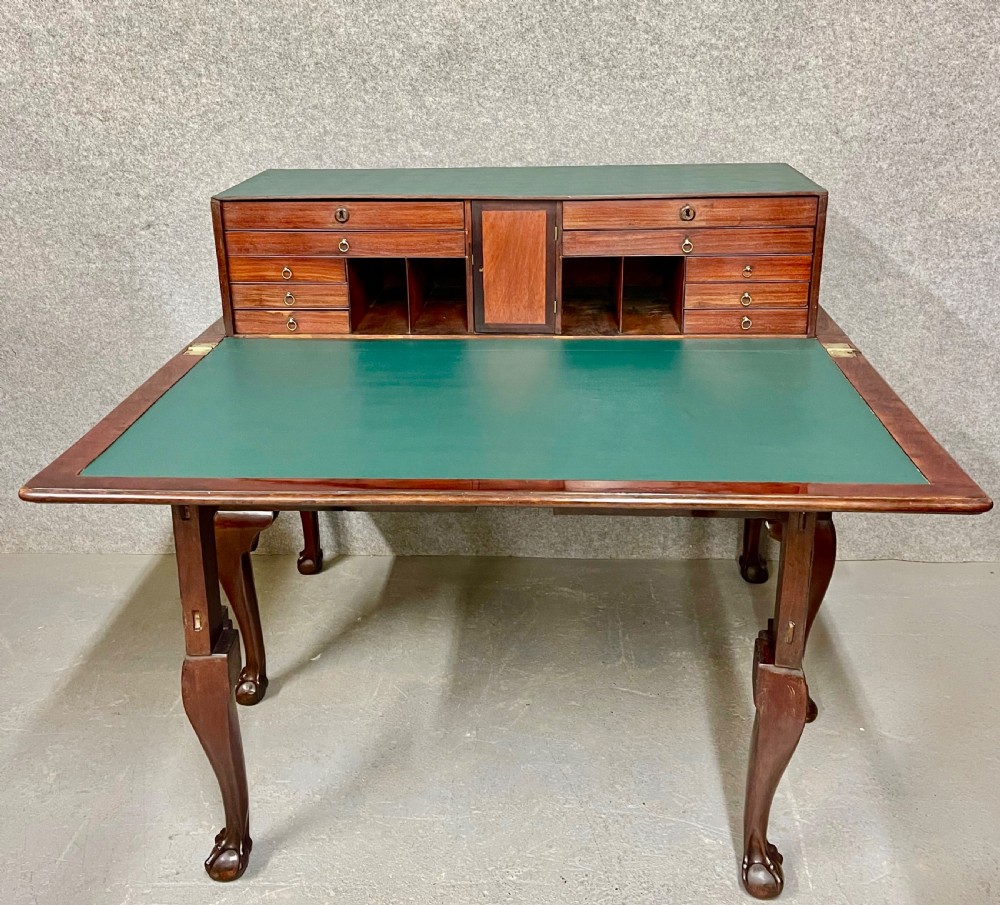 A George III mahogany metamorphic library table featuring a green leather writing surface, a fitted interior of small drawers, and cabriole legs ending in claw and ball feet.