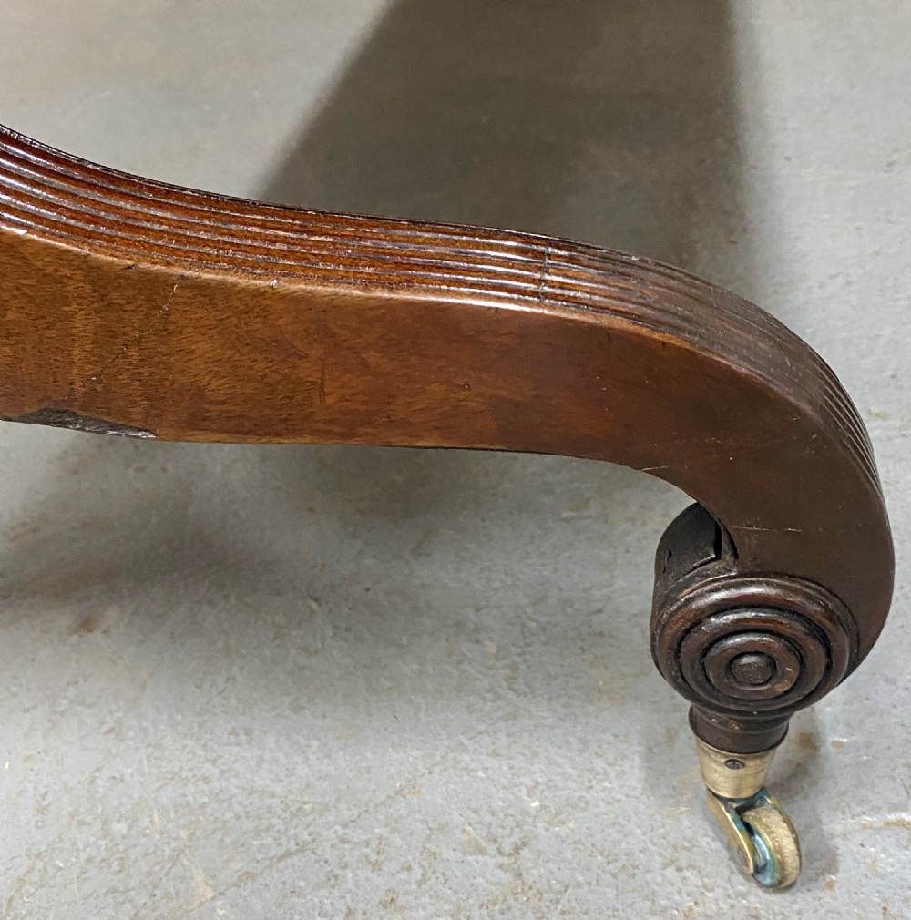 A Regency figured mahogany sofa table featuring two front drawers with brass knobs, drop-down side leaves, a turned stretcher, and reeded sabre legs with brass castors. View VI