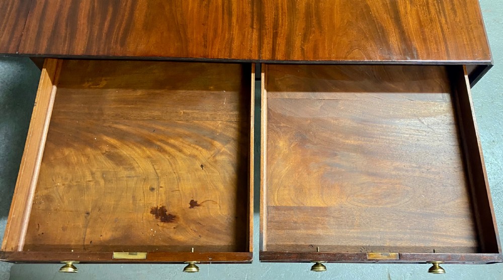 A Regency figured mahogany sofa table featuring two front drawers with brass knobs, drop-down side leaves, a turned stretcher, and reeded sabre legs with brass castors. View IX