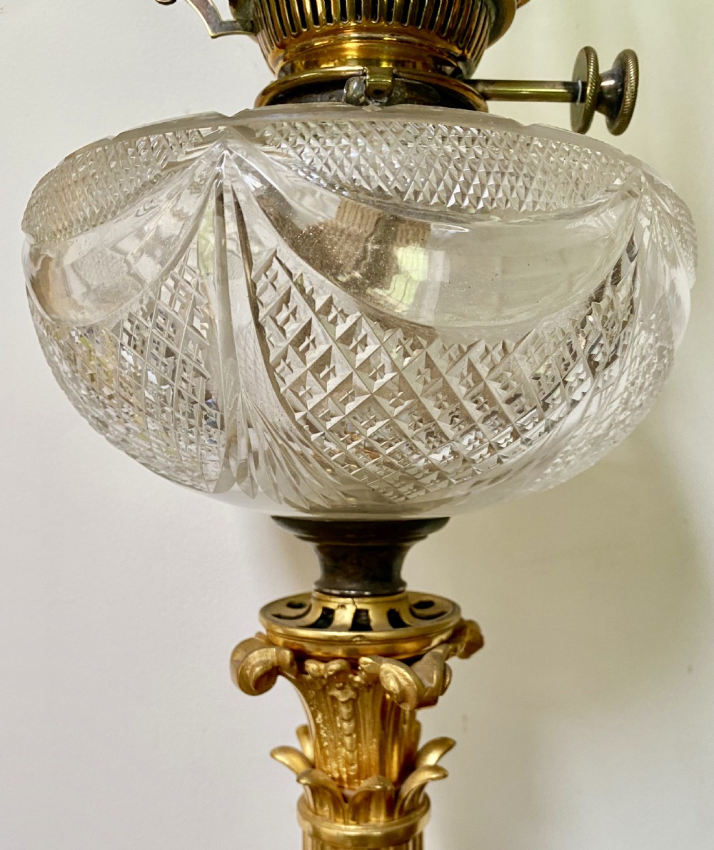 An antique ormolu oil lamp featuring a fluted Corinthian column base, a cut crystal reservoir, and an etched glass shade with a ruffled green rim. View III