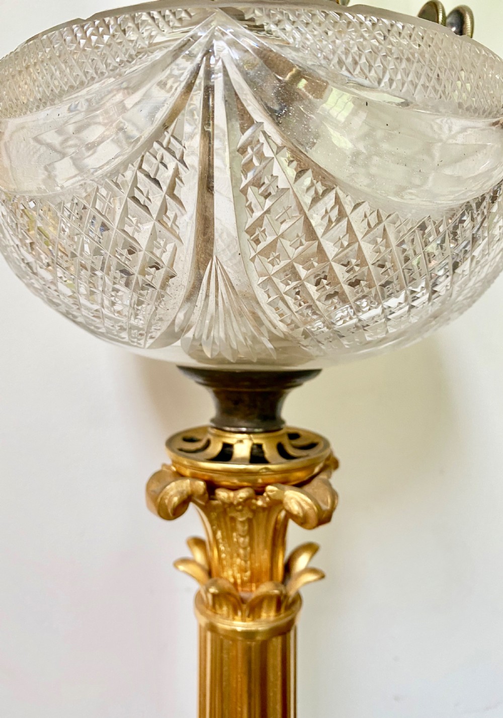 An antique ormolu oil lamp featuring a fluted Corinthian column base, a cut crystal reservoir, and an etched glass shade with a ruffled green rim. View IV