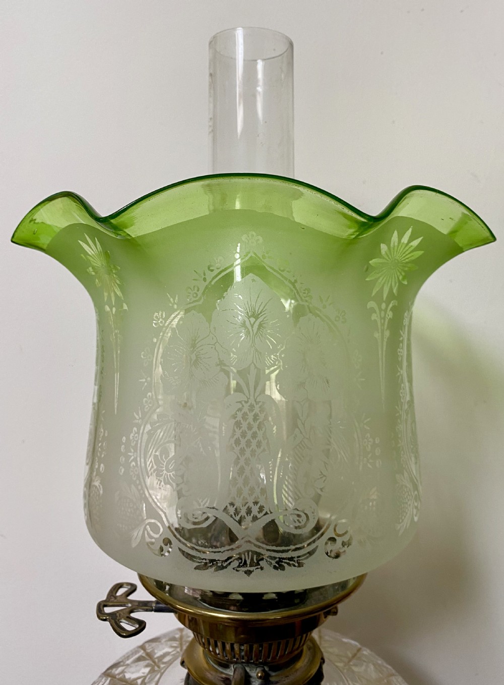 An antique ormolu oil lamp featuring a fluted Corinthian column base, a cut crystal reservoir, and an etched glass shade with a ruffled green rim. View V