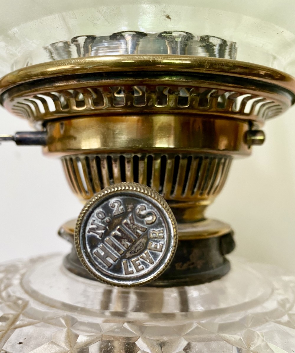 An antique ormolu oil lamp featuring a fluted Corinthian column base, a cut crystal reservoir, and an etched glass shade with a ruffled green rim. View VI