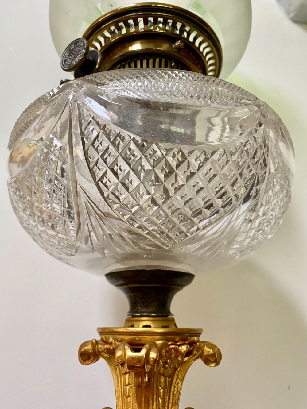 An antique ormolu oil lamp featuring a fluted Corinthian column base, a cut crystal reservoir, and an etched glass shade with a ruffled green rim. View VIII