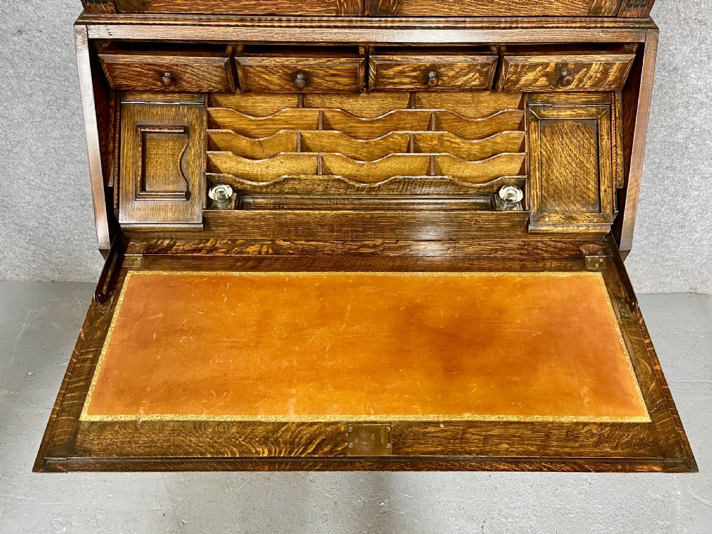 A carved oak bureau bookcase featuring an upper glazed two-door cabinet, a fall-front writing slope with geometric panels, and drawers set upon turned legs. View V