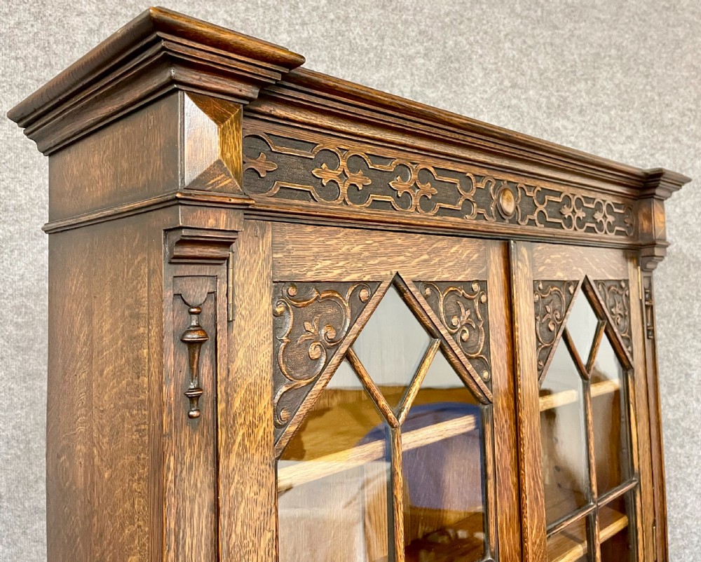 A carved oak bureau bookcase featuring an upper glazed two-door cabinet, a fall-front writing slope with geometric panels, and drawers set upon turned legs. View VI