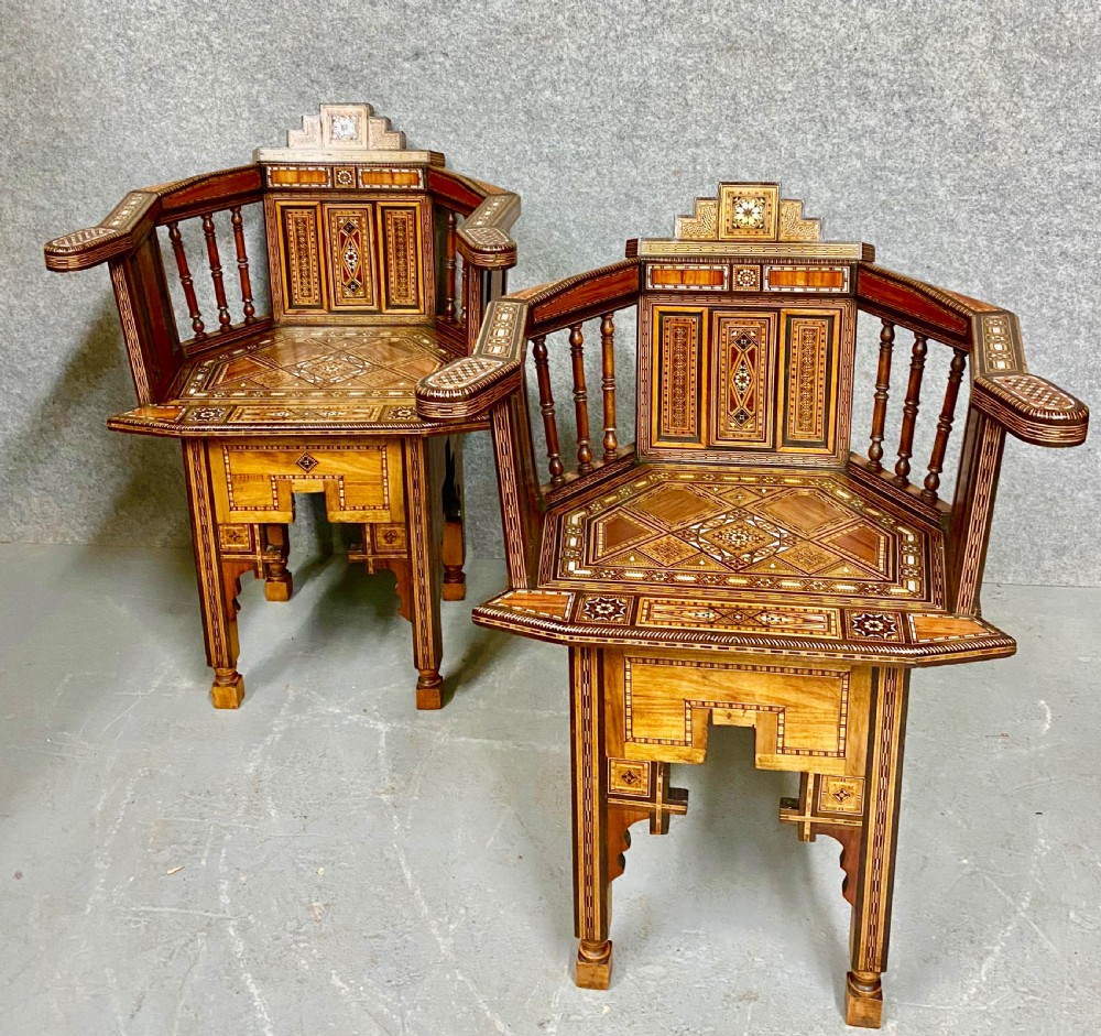 A pair of antique Moorish corner armchairs featuring intricate geometric mother-of-pearl and bone inlay across walnut frames with spindle backrests.