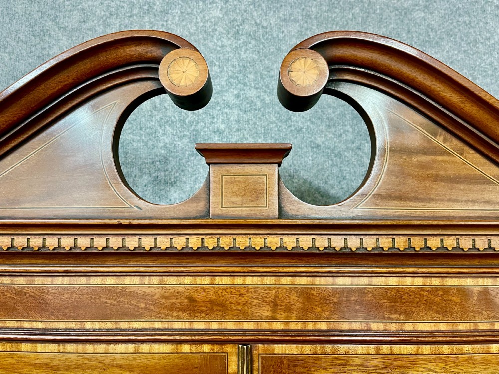 An antique mahogany Sheraton Revival bureau bookcase featuring a swan-neck pediment, astragal glazed upper doors, a slant-front writing bureau, and lower oval-panel cupboards. View V