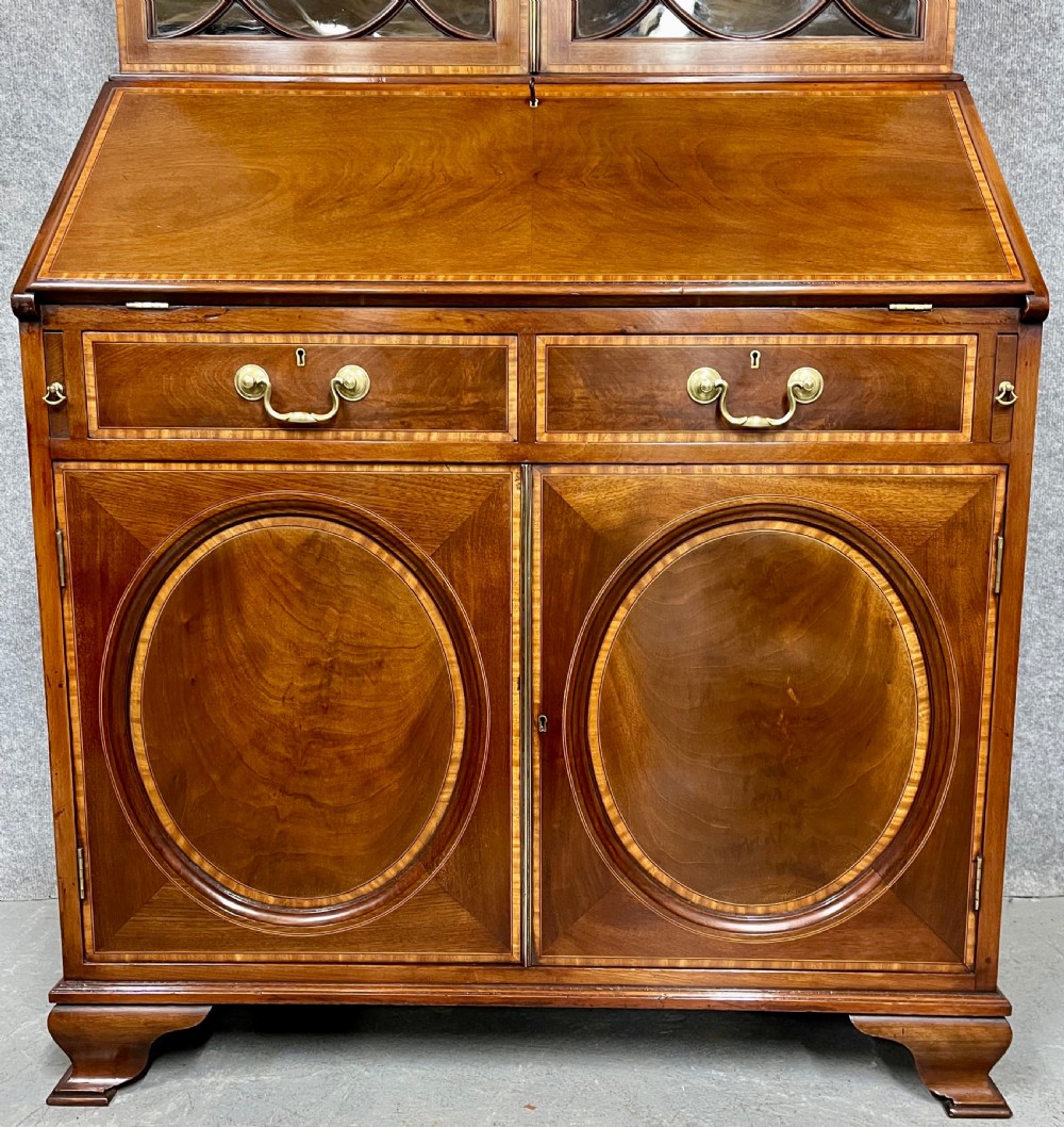An antique mahogany Sheraton Revival bureau bookcase featuring a swan-neck pediment, astragal glazed upper doors, a slant-front writing bureau, and lower oval-panel cupboards. View VIII