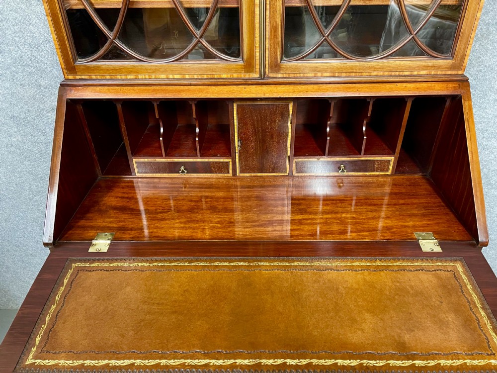 An antique mahogany Sheraton Revival bureau bookcase featuring a swan-neck pediment, astragal glazed upper doors, a slant-front writing bureau, and lower oval-panel cupboards. View IX