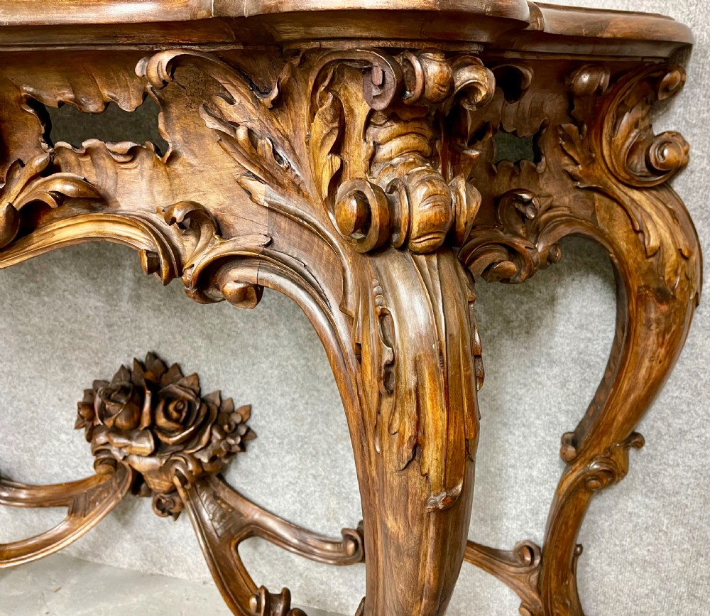 An intricately carved dark walnut console table featuring cabriole legs paired with a tall matching Rococo style arched wall mirror. View VII