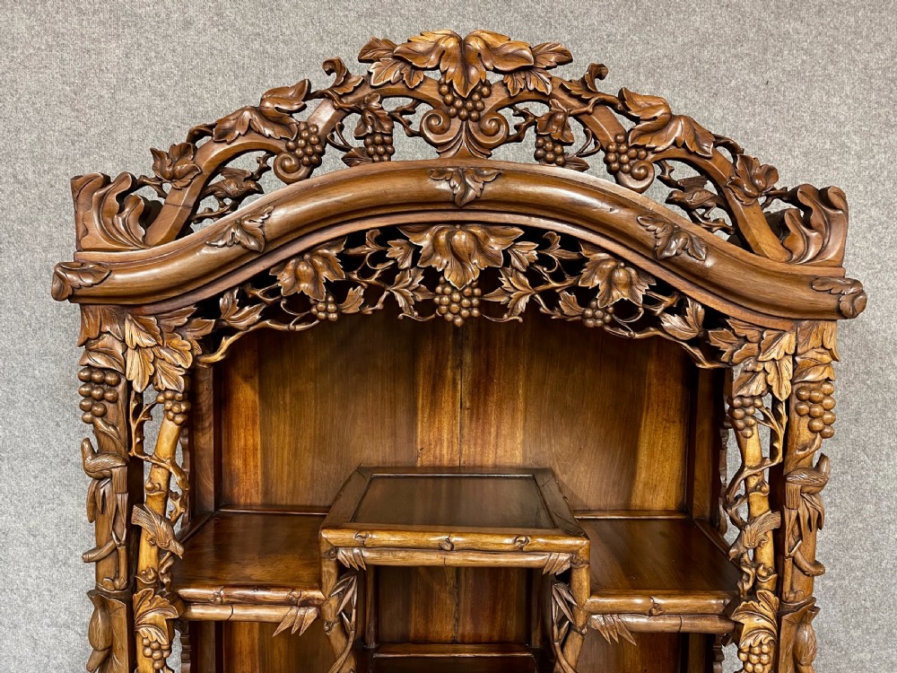 A carved Chinese hongmu open display cabinet featuring asymmetrical shelves framing intricate grapevine and bamboo motifs above a two-door base cupboard. View III