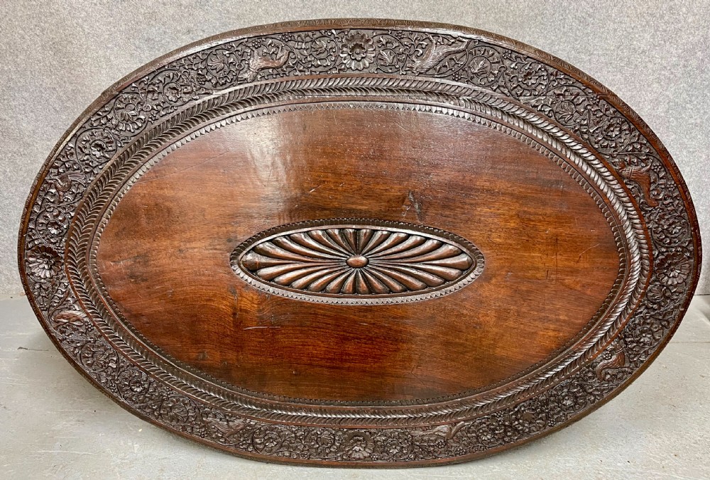 An oval Anglo-Indian dark wood centre table featuring an intricately carved floral border, a central radiating oval medallion, and legs sculpted as elephant heads with white tusks. View III