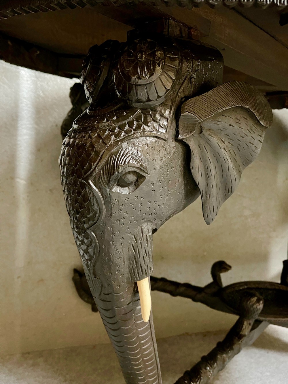 An oval Anglo-Indian dark wood centre table featuring an intricately carved floral border, a central radiating oval medallion, and legs sculpted as elephant heads with white tusks. View VIII