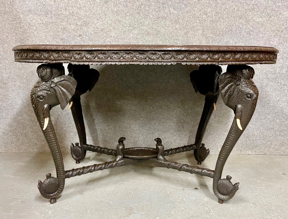 An oval Anglo-Indian dark wood centre table featuring an intricately carved floral border, a central radiating oval medallion, and legs sculpted as elephant heads with white tusks. View XI