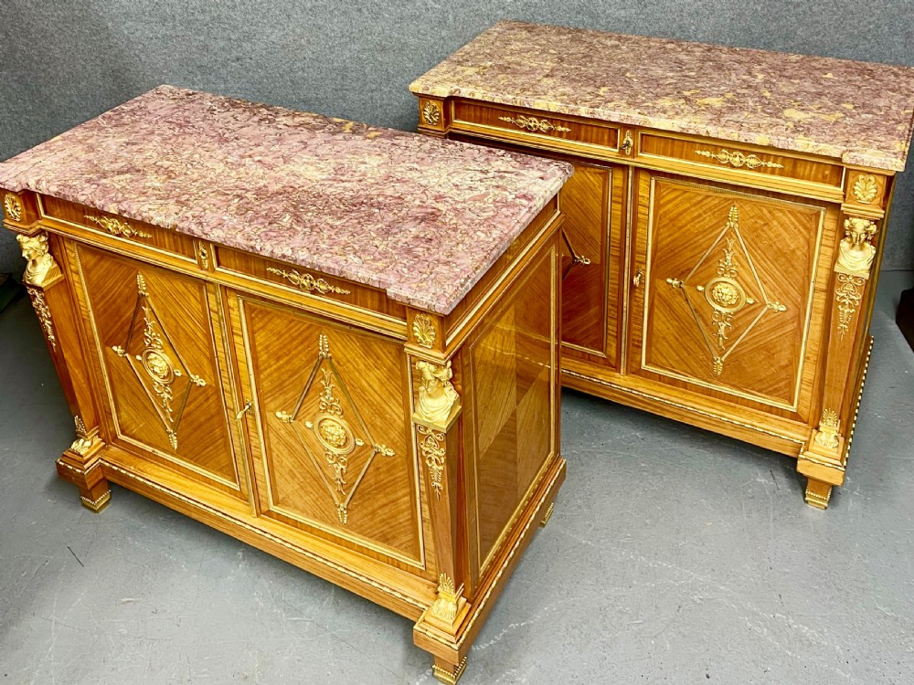 A pair of French Neoclassical side cabinets featuring satinwood parquetry, intricate gilt-bronze mounts, corner bust sculptures, and pink marble tops. View II