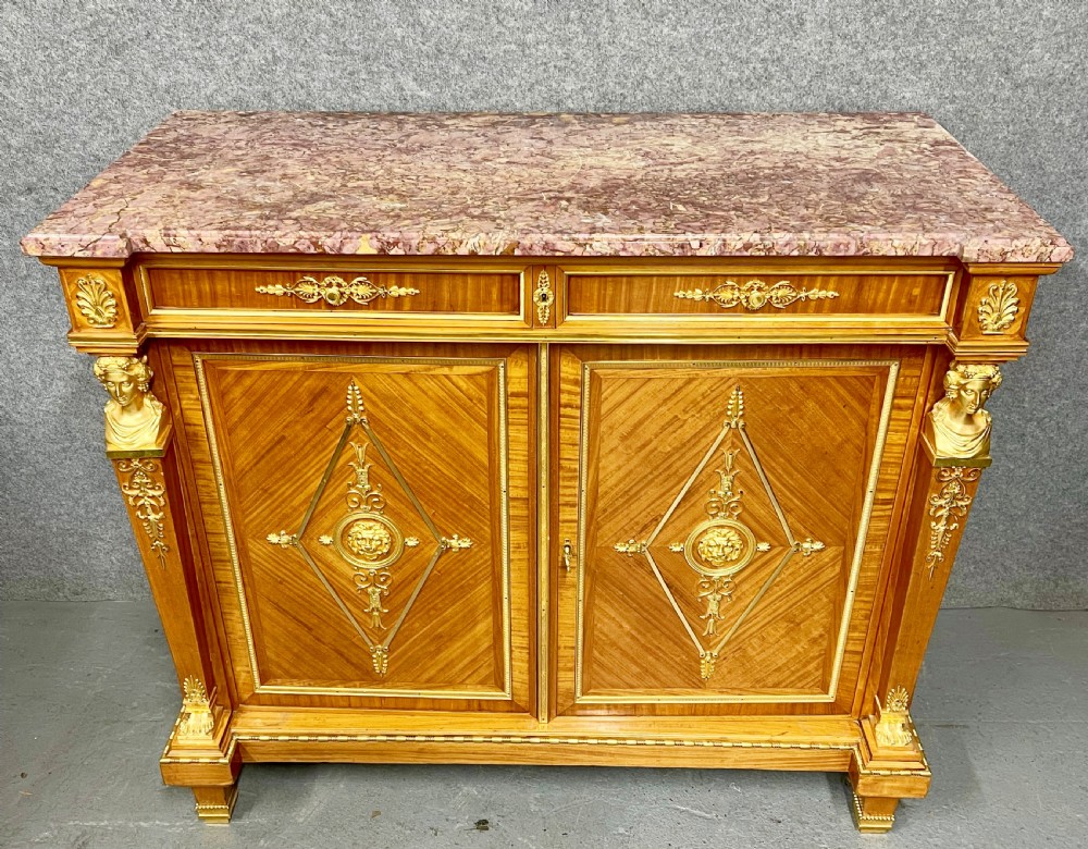 A pair of French Neoclassical side cabinets featuring satinwood parquetry, intricate gilt-bronze mounts, corner bust sculptures, and pink marble tops. View IV