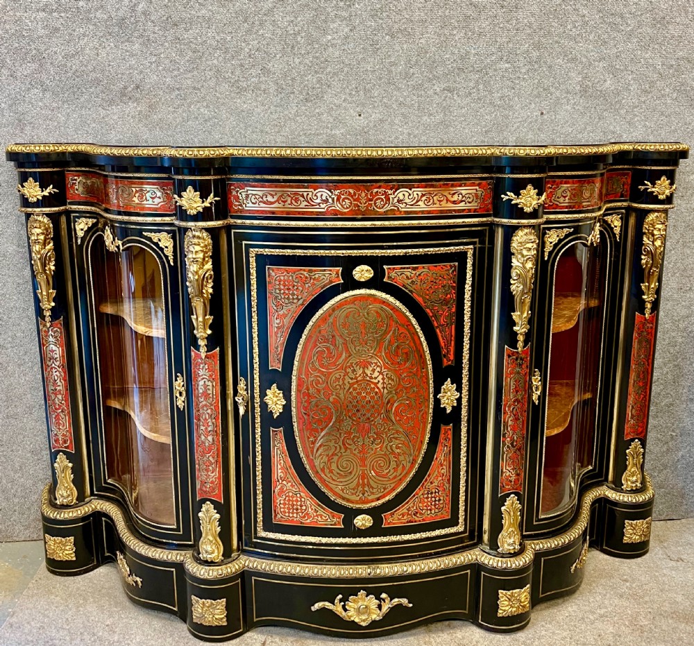 An ebonised serpentine side cabinet featuring red tortoiseshell and brass Boulle marquetry, gilt-bronze ormolu mounts, a central oval-panelled door, and two curved side glazed display sections.