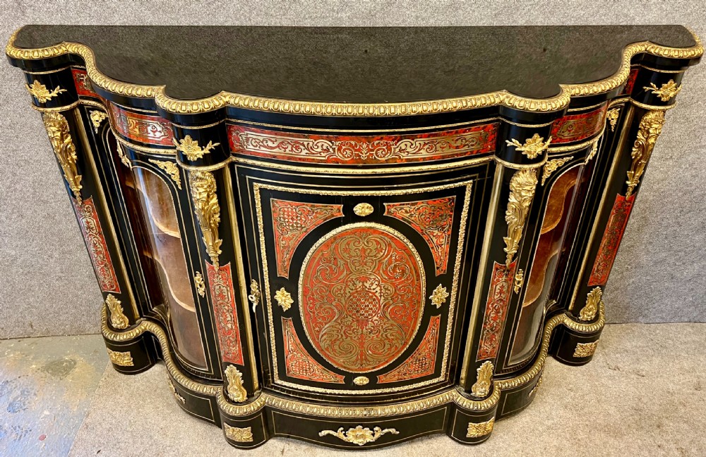 An ebonised serpentine side cabinet featuring red tortoiseshell and brass Boulle marquetry, gilt-bronze ormolu mounts, a central oval-panelled door, and two curved side glazed display sections. View II