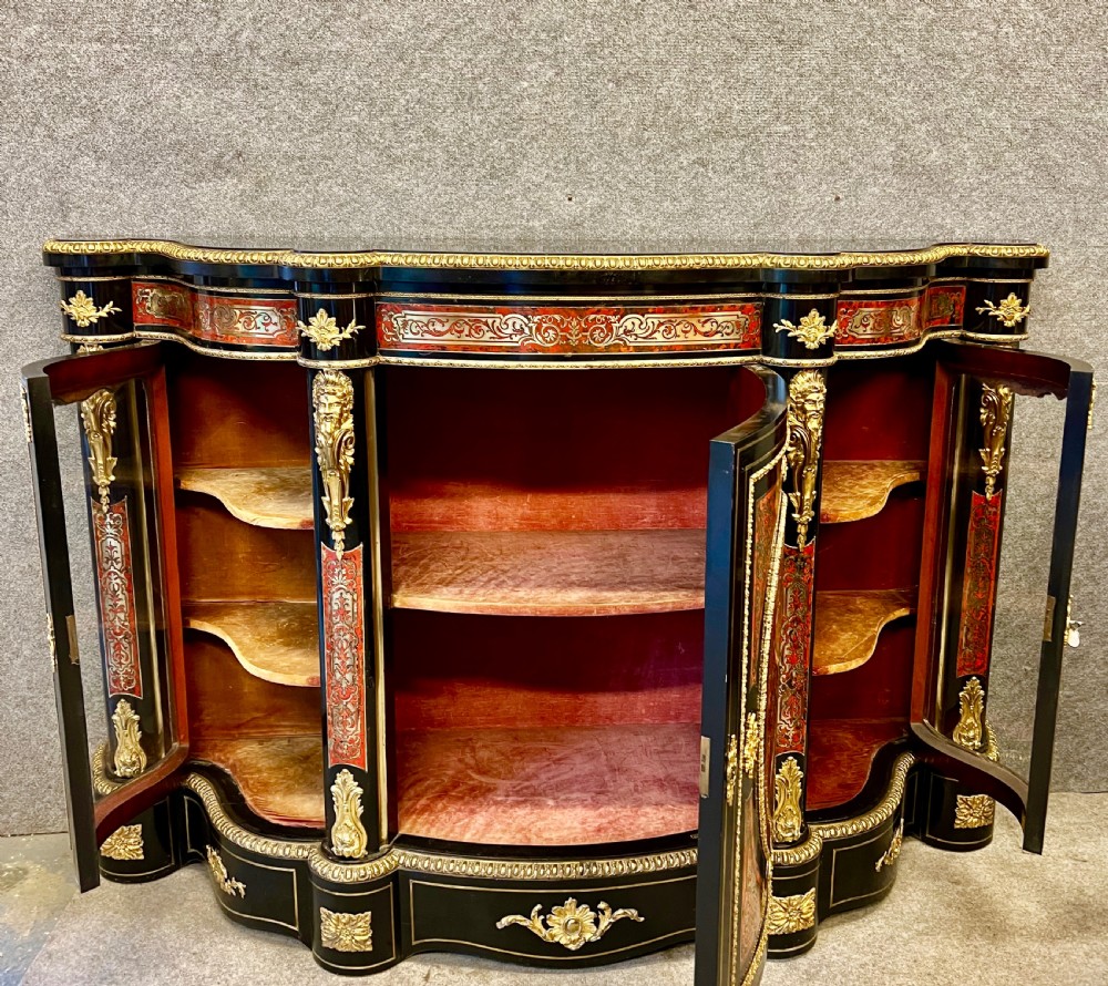 An ebonised serpentine side cabinet featuring red tortoiseshell and brass Boulle marquetry, gilt-bronze ormolu mounts, a central oval-panelled door, and two curved side glazed display sections. View VI