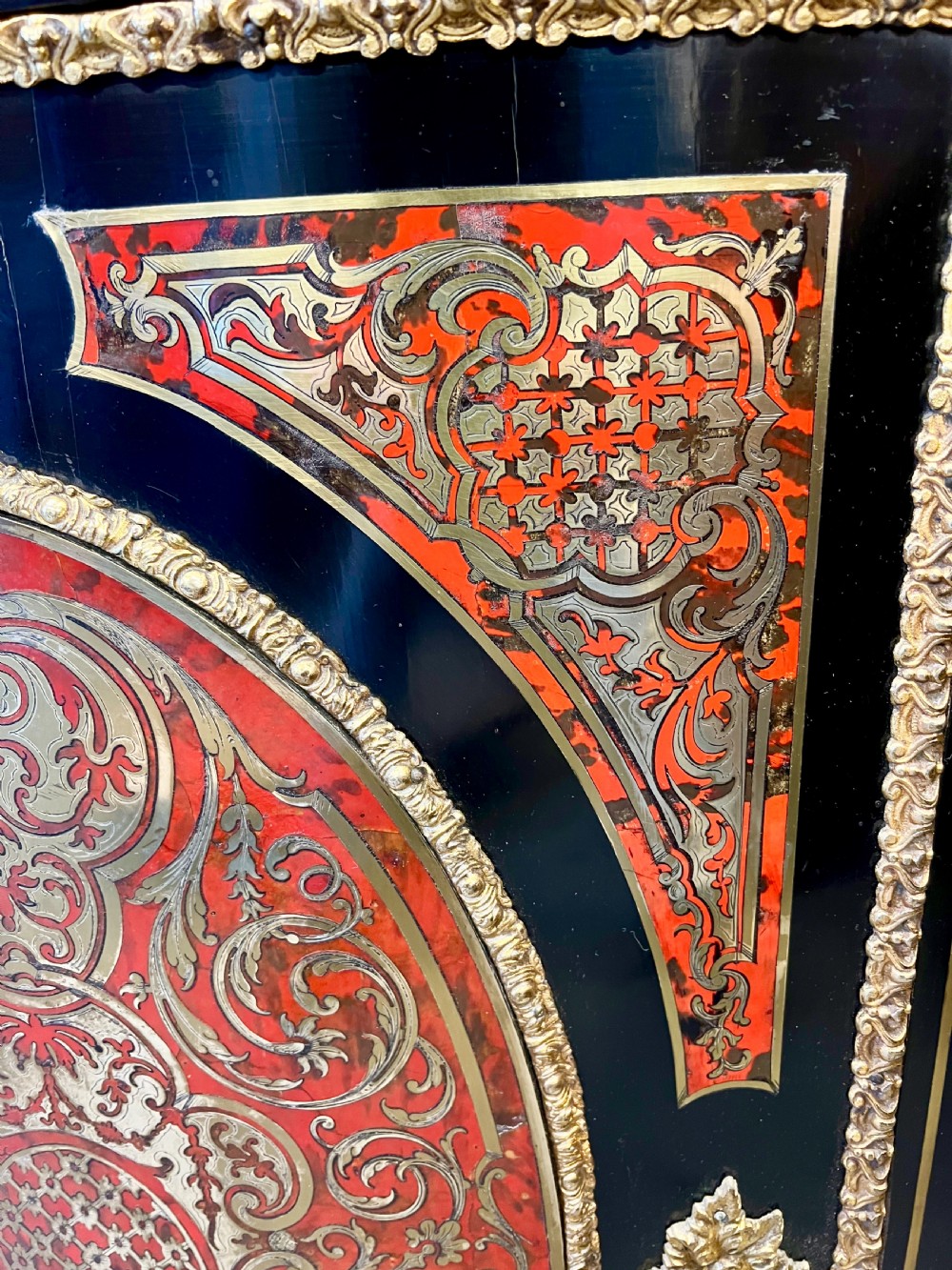 An ebonised serpentine side cabinet featuring red tortoiseshell and brass Boulle marquetry, gilt-bronze ormolu mounts, a central oval-panelled door, and two curved side glazed display sections. View X