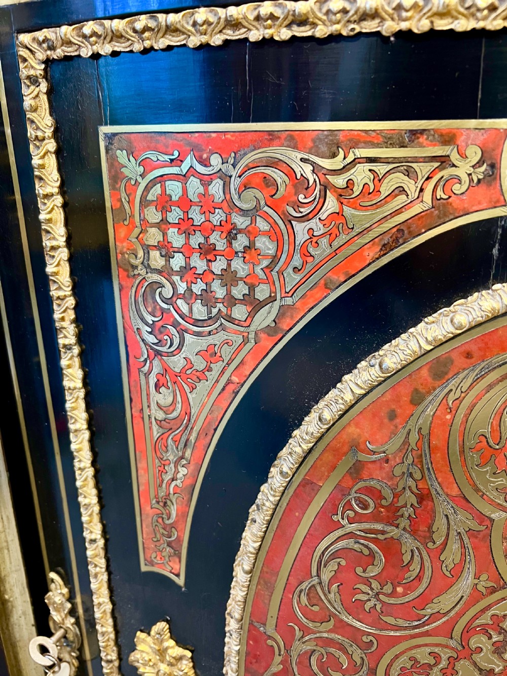 An ebonised serpentine side cabinet featuring red tortoiseshell and brass Boulle marquetry, gilt-bronze ormolu mounts, a central oval-panelled door, and two curved side glazed display sections. View XI