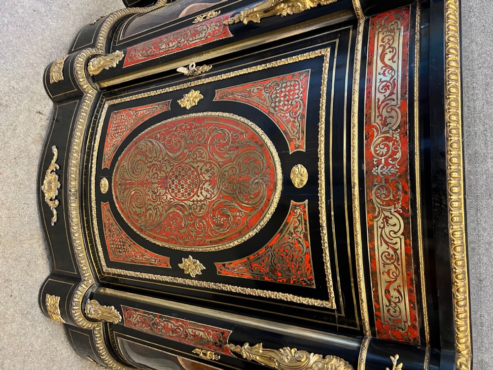 An ebonised serpentine side cabinet featuring red tortoiseshell and brass Boulle marquetry, gilt-bronze ormolu mounts, a central oval-panelled door, and two curved side glazed display sections. View XII