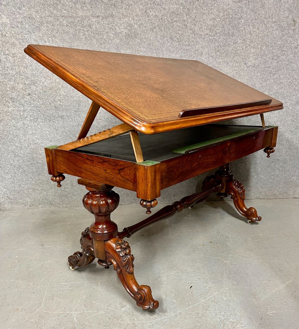 An antique rosewood library architects desk featuring an adjustable slanted writing top raised on ratchets over a carved dual-pedestal base with brass castors.