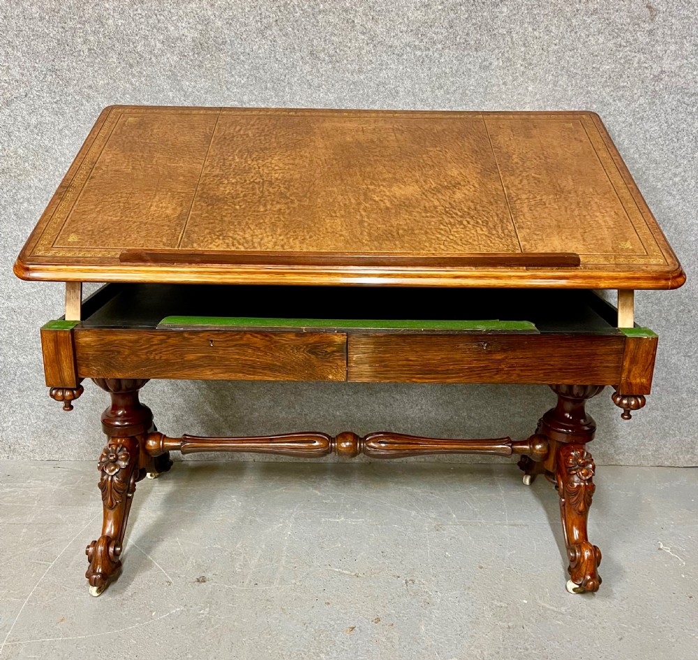 An antique rosewood library architects desk featuring an adjustable slanted writing top raised on ratchets over a carved dual-pedestal base with brass castors. View V