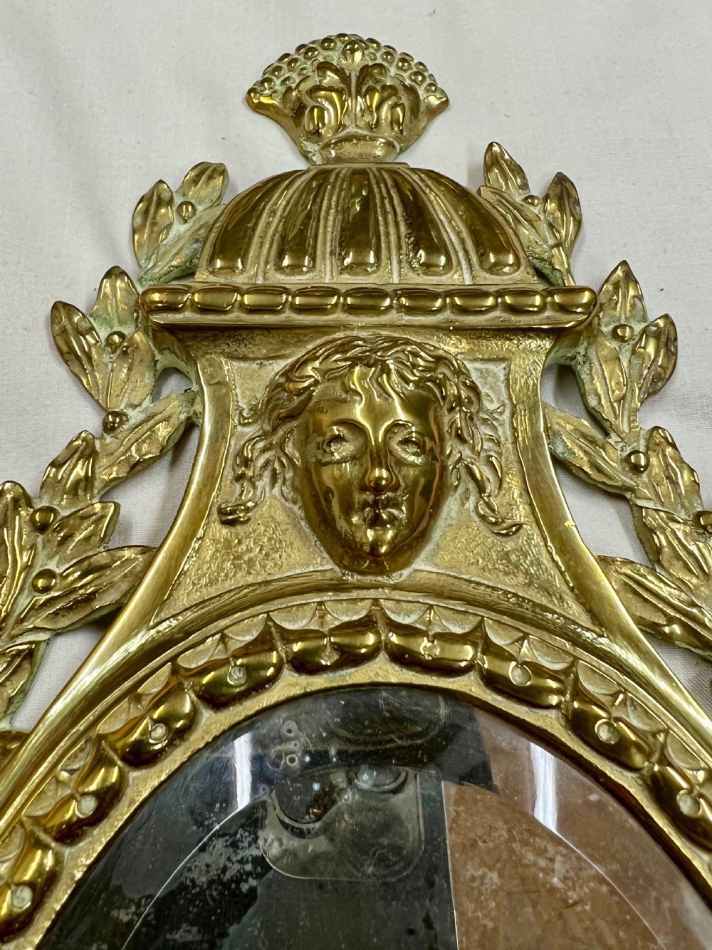 A pair of gilt brass girandole wall mirrors with oval bevelled glass plates, classical mask motifs, acanthus scrolls, and twin candle holders. View III
