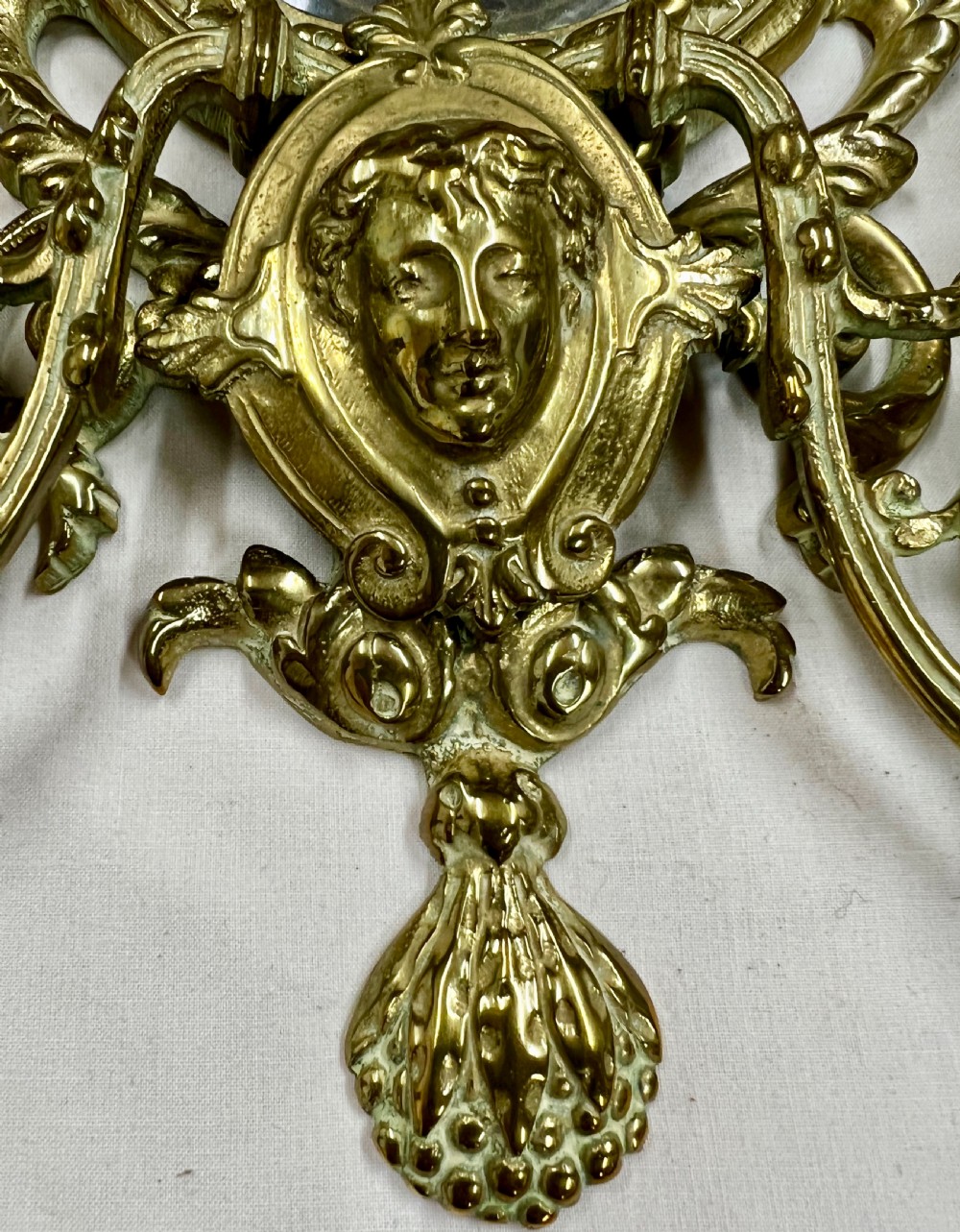 A pair of gilt brass girandole wall mirrors with oval bevelled glass plates, classical mask motifs, acanthus scrolls, and twin candle holders. View V