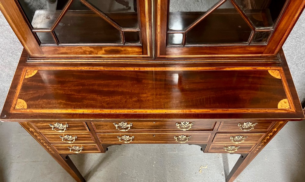 A Sheraton Revival mahogany cabinet featuring a swan-neck pediment, glazed upper doors with geometric bars, inlaid satinwood stringing, and multiple drawers set on tapered square legs. View III