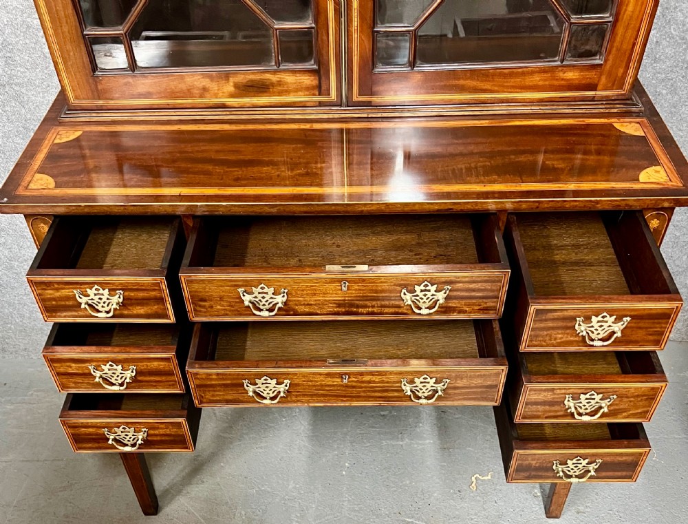A Sheraton Revival mahogany cabinet featuring a swan-neck pediment, glazed upper doors with geometric bars, inlaid satinwood stringing, and multiple drawers set on tapered square legs. View IV