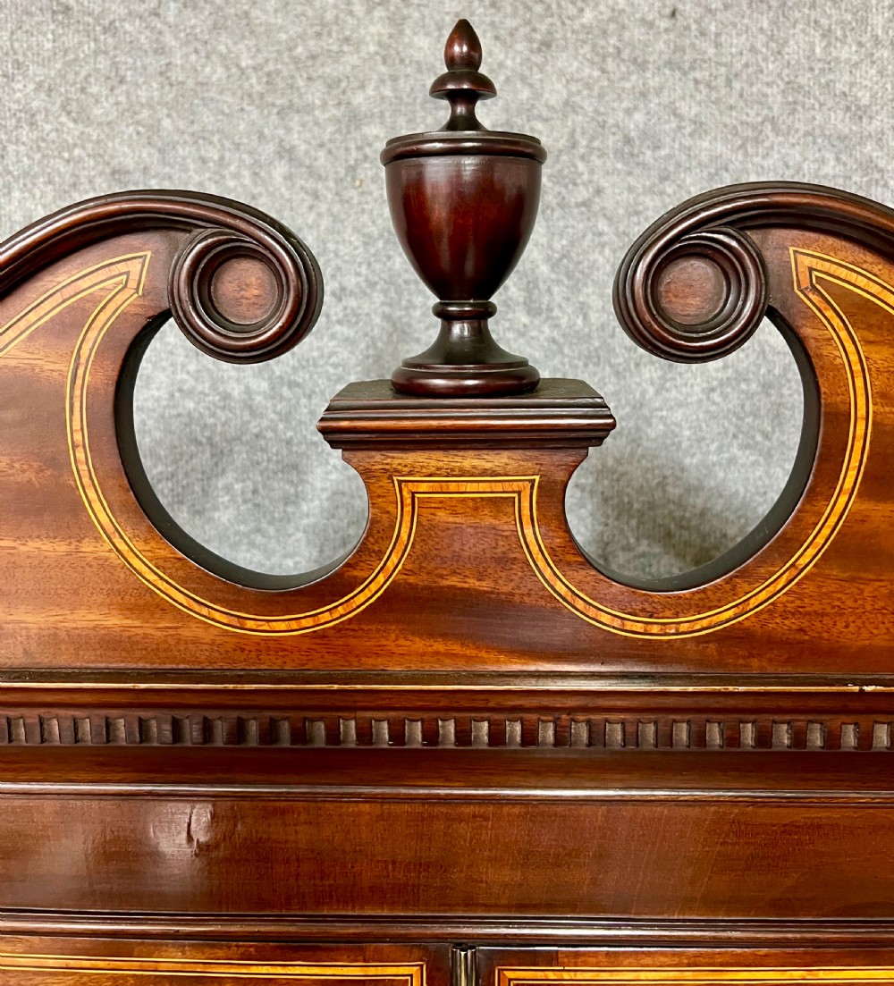 A Sheraton Revival mahogany cabinet featuring a swan-neck pediment, glazed upper doors with geometric bars, inlaid satinwood stringing, and multiple drawers set on tapered square legs. View VIII